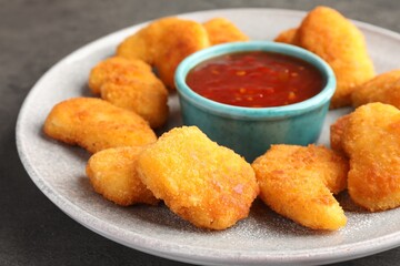 Plate with hot chili sauce and nuggets on grey table, closeup