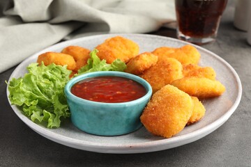 Plate with hot chili sauce, lettuce and nuggets on grey textured table, closeup