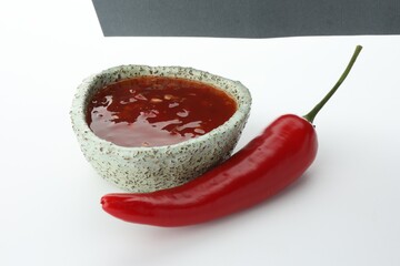 Hot chili sauce in bowl and pepper on white background