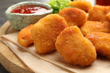 Board with nuggets and hot chili sauce on table, closeup