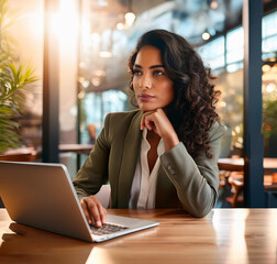 Fototapeta premium Businesswoman working on a laptop at a coffee shop table, thinking of a business plan