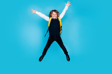 Full size photo of small schoolkid boy jump rejoice wear uniform isolated on blue color background