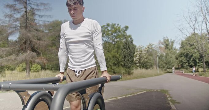 A man engages in outdoor fitness by performing dips on parallel bars in a park on a sunny day, demonstrating fitness lifestyle and dedication..