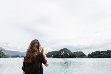 European girl in headphones listens to music by the lake while sitting on the pier.
