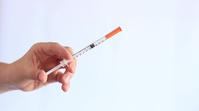 Insulin syringe. A woman's hand holds a syringe on a white background, close-up. Insulin syringe for diabetes. Diabetes treatment. Medicine and health concept