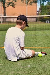 A lonely boy sitting on a local tennis court with a racket and a ball © Gosia