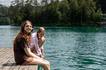 two girls are sitting on a wooden pier on a hot day on lake bled. they dipped their feet in the water and enjoyed the summer holidays