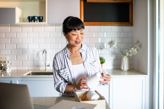 Happy Asian woman opening package in the kitchen