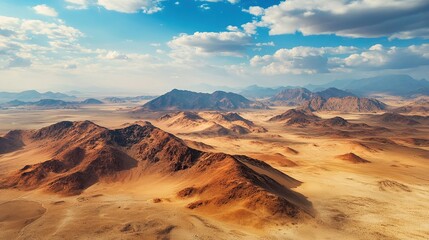 Naklejka premium A vast, sandy desert landscape with a range of brown mountains stretching across the horizon under a bright blue sky with white fluffy clouds.