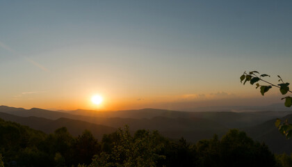 Sun setting over mountains and forested landscape.