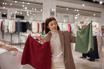 Young woman asking for help in need advice on choosing skirt at fashion store