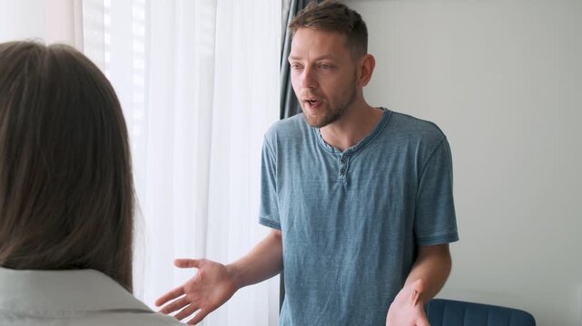 Man arguing with woman in heated conversation, expressing frustration with hand gestures. Angry worried young couple quarreling and arguing at home. Relationship crisis, family conflict, breakup