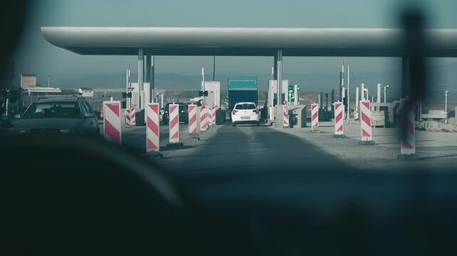 Pov from windshield of car driving down a highway road with a lot of traffic cones pay toll station in the background