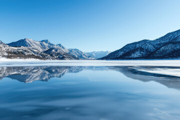 A Majestic Frozen Lake: Crystal Clear Reflections Under a Brilliant Blue Sky Enhance the Serene Winter Landscape