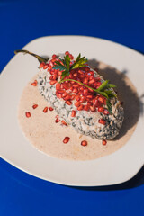 Detail of chile en Nogada, traditional Mexican food in the month of September served on a white plate on a blue table.