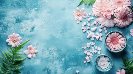 Flat lay of pink flowers and bath salts on blue background, perfect for spa or wellness themes with a serene and relaxing ambiance.