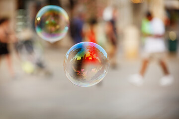 Soap bubble float at air reflect colorful scene in lively street