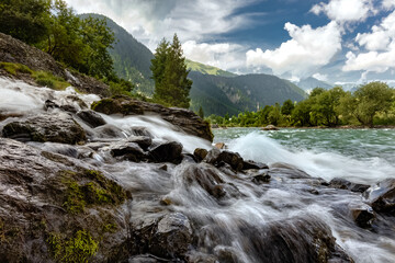 Waterfall among the himalaya mountains with green forest and a river full of rocks.