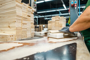 Worker handling stacks of wooden planks in a woodworking factory, preparing materials for further processing under industrial lighting