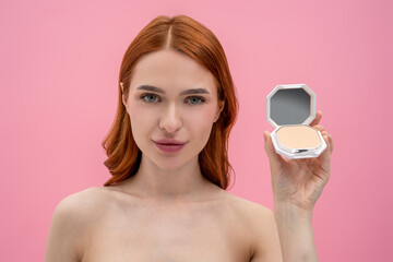 Ginger woman with bare shoulders with cream powder in hands