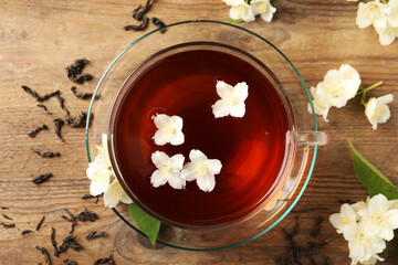 Hot jasmine tea in cup and flowers on wooden table, flat lay