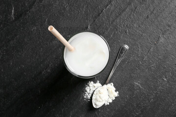 Delicious protein shake in glass and spoon with powder on black table, top view