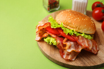 Delicious burger with bacon, tomato and lettuce on green background, space for text