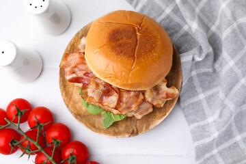 Delicious burger with bacon, greens and tomatoes on white table, flat lay