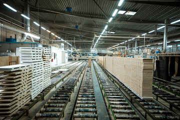 Obraz premium A large woodworking factory with stacks of freshly cut timber panels ready for processing, showcasing industrial efficiency and precision in a well-lit manufacturing environment