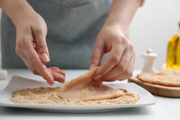 Woman making schnitzel at white table, closeup