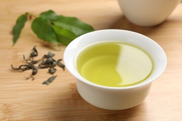 Refreshing green tea in cup and leaves on wooden table, closeup
