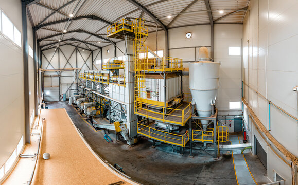 A manufacturing facility with a modern woodworking machine processing wooden planks. The control panel is illuminated, showing active production metrics, surrounded by stacked wood