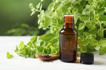 Essential oil in bottle, dry herbs and oregano leaves on white wooden table against blurred green background, closeup