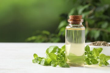 Essential oil in bottle and oregano leaves on white wooden table against blurred green background,...