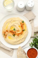 Delicious hummus with olive oil, chickpeas and paprika served on white wooden table, flat lay