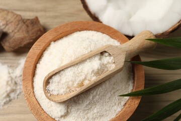 Fresh coconut flour in bowl, scoop, nut and palm leaf on wooden table, above view