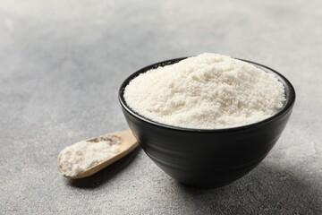 Coconut flour in bowl and spoon on light grey table, closeup