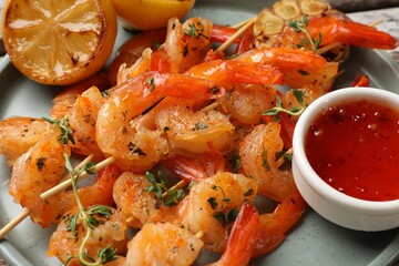 Delicious grilled shrimp skewers, sauce and lemon on plate, closeup