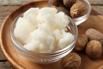 Shea butter in bowl and nuts on wooden table, closeup