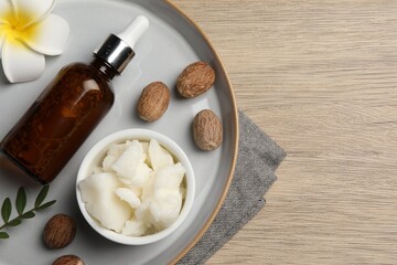 Shea butter, bottle, flower and nuts on wooden table, top view. Space for text
