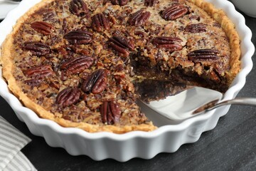 Delicious pecan pie in baking dish and cake server on dark gray textured table, closeup