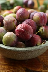Ripe plums in bowl on wooden table, closeup