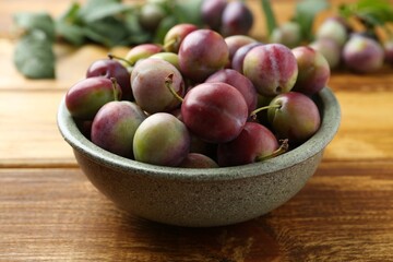 Ripe plums in bowl on wooden table, closeup