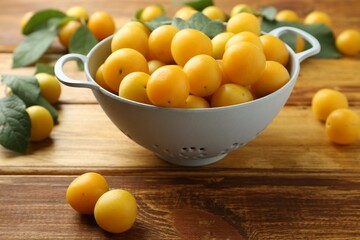 Tasty ripe plums and leaves in colander on wooden table, closeup