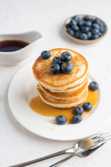 Stack of pancakes with blueberries and maple syrup on white plate. Breakfast meal