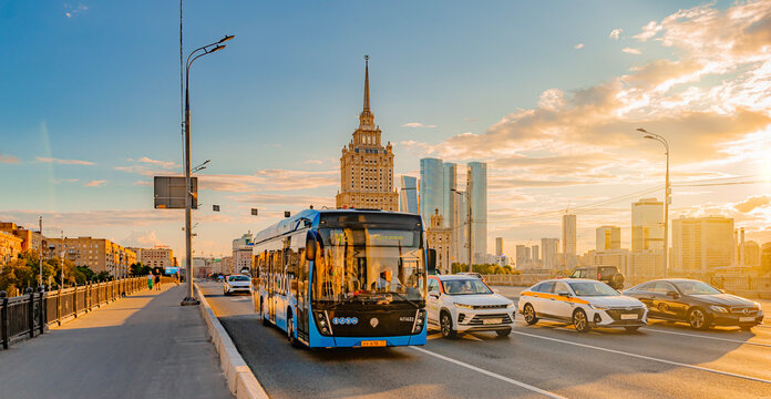 Moscow, Russia, August 12, 2024: Electrobus drive down the street in Moscow, front side view. Electric bus in motion at sunset. Hotel Ukraine in the background
