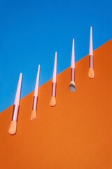 A row of five brushes with pink handles is displayed on a blue and orange background. Cosmetic concept