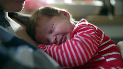 Peaceful moment of a newborn baby sleeping on mother’s chest in a red striped onesie, showcasing family bonding