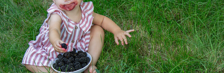 little girl eats blackberry on the background of nature. Selective focus