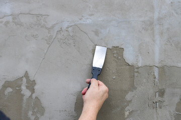 A person is holding a trowel and applying a layer of cement to a wall